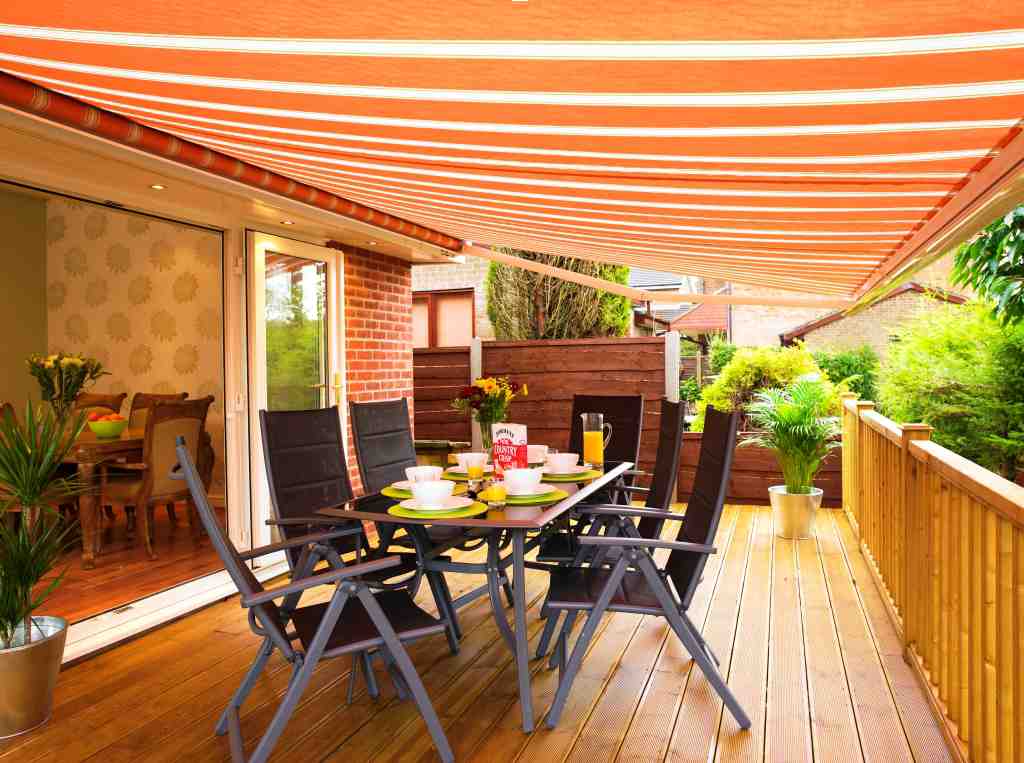 Domestic Awning on a raised patio decking. Orange and white in colour and covering an outdoor dining table and chairs.